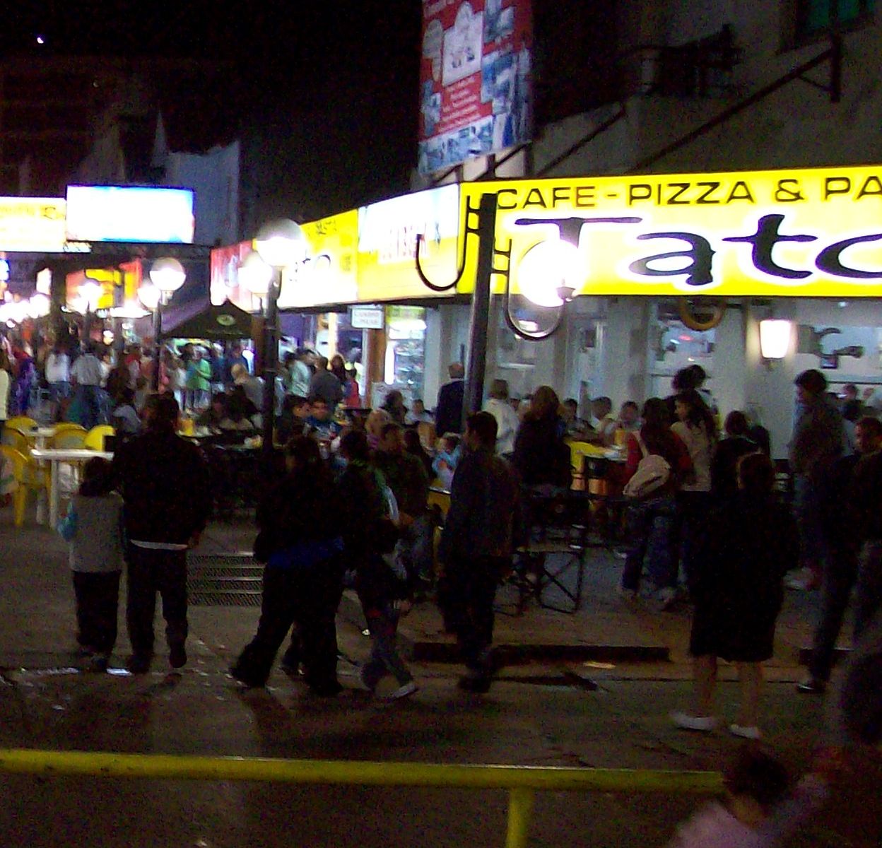 El centro de Mar de Ajó de noche, en temporada, con las mesas y el cartel de Tato
